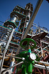 Green pressure measuring device (gauge, manometer) Grey oil distillation tower (refining columns), pipelines on background. Oil processing plant on deep blue sky. Taraz city. Kazakhstan.