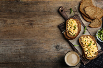 Tasty scrambled egg sandwiches served on wooden table, flat lay. Space for text