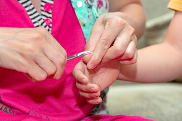 Obraz na płótnie Canvas Mom cuts the child's fingernails with small children's scissors. Care and guardianship of children by parents.