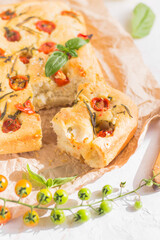 Traditional italian focaccia bread with tomatoes and rosemary in mental baking tray . On the beige brown paper and white concrete background.