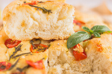 Traditional italian focaccia bread with tomatoes and rosemary in mental baking tray . On the beige brown paper and white concrete background.