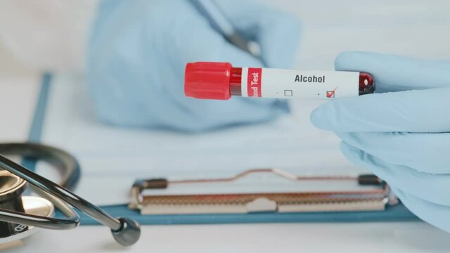 Doctor or laboratory technician holds in one hand laboratory positive blood sample for an alcohol test, other handwriting down results to patients medical records. Laboratory medical diagnostics
