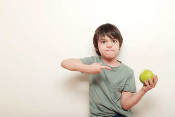 niño con expresión de molestia señalando con el dedo la manzana verde que sujeta con la otra mano sobre fondo blanco