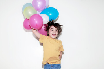 Fototapeta na wymiar niño de 5 a 7 años brincando con una sonrisa mientras sostiene globos de colores sobre un fondo blanco 