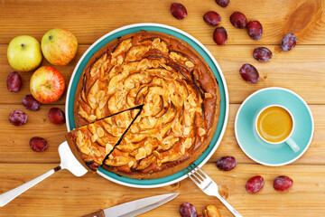 Homemade pie with apples and plums with almond petals and cup of coffee espresso on wooden table. Top view.