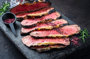 Traditional Commonwealth Sunday roast with sliced cold cuts roast beef with herbs and salt as close-up on a rustic charred wooden board