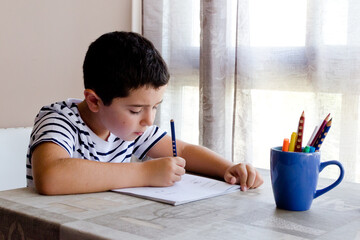 Niño con camiseta de rayas concentrado y escribiendo mientras aprende en casa