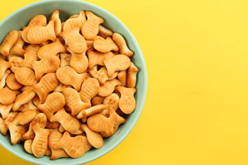 Delicious goldfish crackers in bowl on yellow background, top view. Space for text