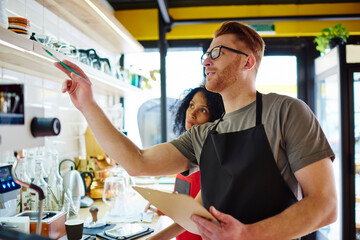 Owner pointing at shelf working with colleague in cafe