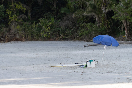 Praia do Engenho, litoral Norte do Estado de S&atilde;o Paulo. Guarda-sol azul, prancha de surf e geladeira de isopor deixados no canto da praia. Praia vazia. 