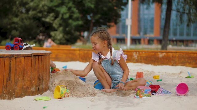 Little girl playing with plastic toys and buckets in sandbox at residential area