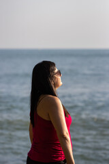 Fototapeta na wymiar Mulher brasileira de cabelos negros usando camiseta vermelha, sentindo a brisa do mar em praia do litoral de São Paulo 