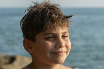 Retrato menino brasileiro com sol no rosto em praia do litoral de São Paulo.