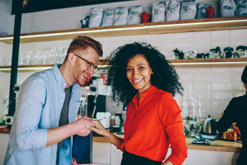Handshaking of multicultural successful owners of cafeteria during great job in development business startup.Positive african american young woman teamworking with professional male manager in cafe
