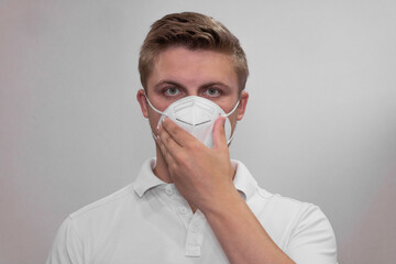 A young man in a white mask on a white background holds his hand to his face