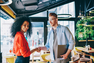 Caucasian professional male manager handshaking dark skinned female owner of cafeteria for great collaboration.Portrait of african american administrator working in team with professional employee
