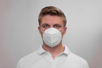 A young man in a white mask on a white background holds his hand to his face