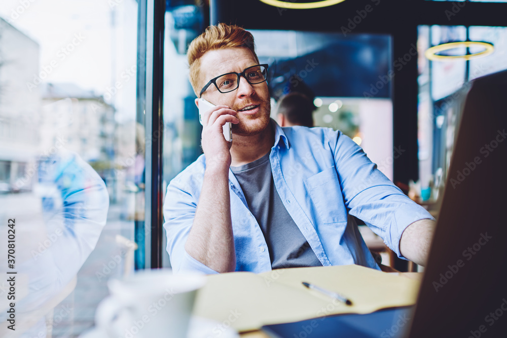 Poster caucasian hipster guy spending time for calling to clients of own application on laptop computer che