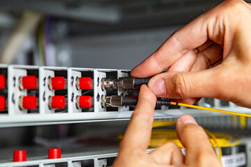 A man inserts a yellow black fiber optic cable into a switch. Hands close up. Horizontal orientation. 
