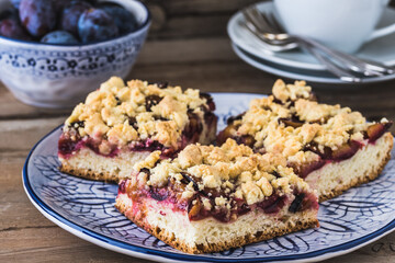Three pieces of plum cake with crumble on a bluewhite plate  on a wooden table