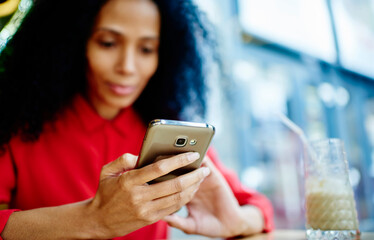 Fototapeta na wymiar African American female sitting with coffee and messaging via smartphone