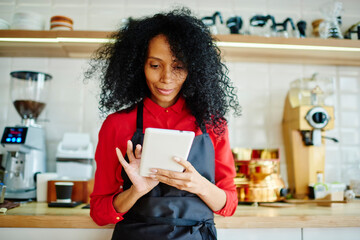 Black barista browsing tablet in cafe