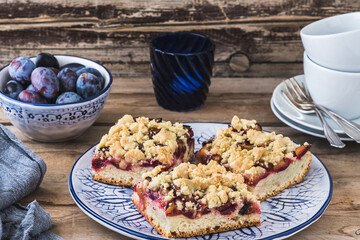 Three pieces of plum cake with crumble on a bluewhite plate on a wooden table