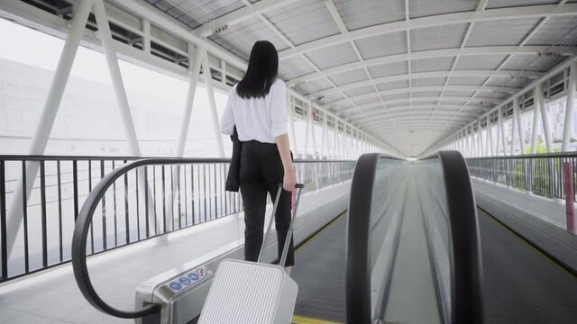 Young asian woman business wearing white shirt live in airport, She walk to escalator of footbridge and stop to standing with her luggage. Slow Motion Shot.