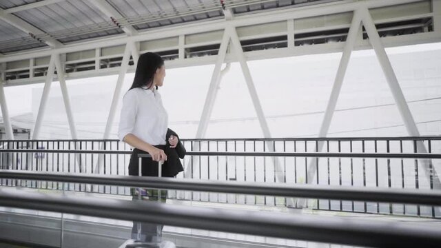 Young asian woman business wearing white shirt live in airport, She standing and slide on escalator of footbridge with her luggage. Slow Motion Shot.