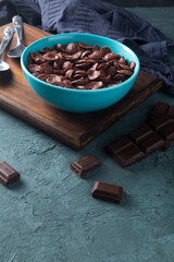 Delicious and healthy chocolate cereal in bowl with chocolate pieces laid down next to it in a dark setting