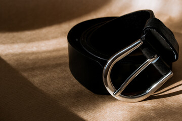 black belt with silver buckle on kraft paper, stylish belt with sun rays, shadow