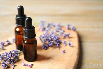 Bottles of essential oil and lavender flowers on wooden table. Space for text