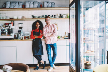 Portrait of positive successful hipster owner of cafe developing startup business with professional african american barista.Partnership of dark skinned waitress and prosperous hipster guy