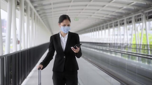 Young asian woman business live in airport, She wearing face mask for protect virus air pollution on safety travel and walk in to audience suddenly she stop to talk with her mobile. Slow Motion Shot.