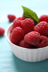 Delicious ripe raspberries in bowl on light blue wooden table, closeup