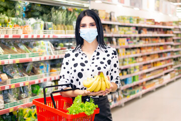 young woman in a disposable medical mask is shopping at the supermarket. buying fruit