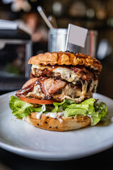 Bacon burger with beef patty and green salad on wooden table in cafe.