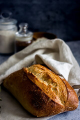 Homemade sourdough bread on a dark table with a napkin, next to flour. Loaf of freshly baked bread close up, vertical background