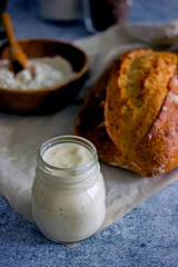 Bread starter sourdough in a glass jar on a dark background, near bread and flour, vertical background, close-up