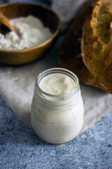 Bread starter sourdough in a glass jar on a dark background, near bread and flour, vertical background, close-up