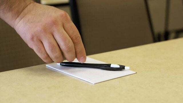 Male hand is putting a pen onto notepad. Side shot of male hand as it puts down a pn onto a notepad.
