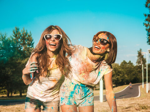 Two happy beautiful girls making party at Holi colors festival in summer time.Young smiling women friends having fun after music event at sunset. Positive models going crazy in sunglasses at sunset