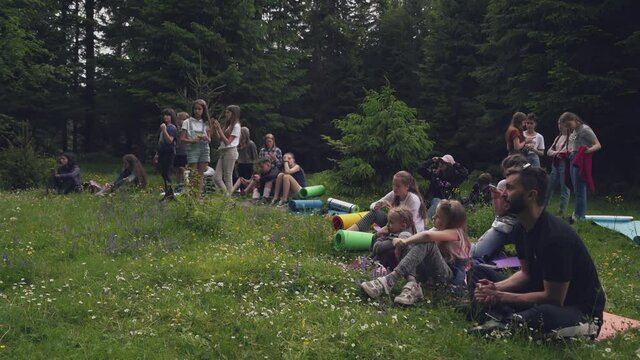Teens sitting on mats in forest.