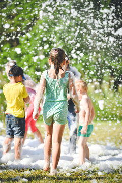 Young people in the foam. A foam party. Group of children having fun, enjoying and dancing at a foam party in aquapark. Outdoor view of foam machine.