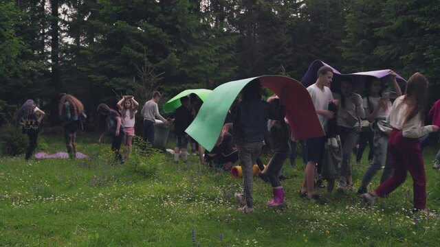 Teens using mats as umbrellas in forest.