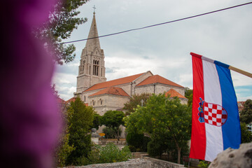 Obraz na płótnie Canvas Closeup of the Croatian flag waving in the wind with the church in the village of Selca, Croatia in the background. Celebrating Croatian victory in the war of independence