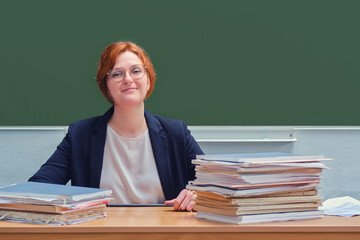 Happy teacher smiling while sitting at a desk, copy space on a green background