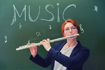 Woman music teacher plays the flute at the blackboard, copy space. Cute school teacher on green background, close up © Андрей Журавлев