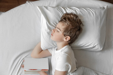 A teenage boy sleeps in bed with a book. Everyday life of a schoolboy. Top view.