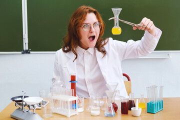 Analyzes, tests and research in the school laboratory. Surprised teacher holding a bottle of yellow...